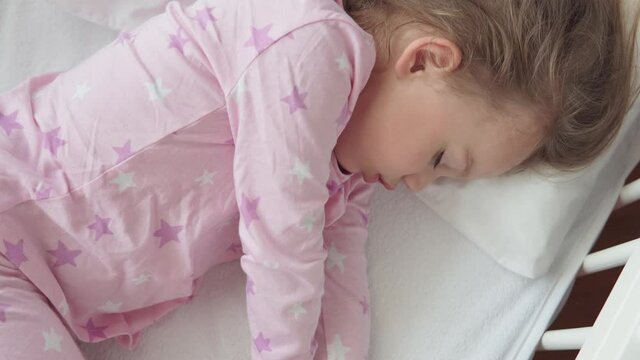 close up authentic cute caucasian little preschool child girl sleep sweetly in white crib on pajama in bedroom during lunchtime. kid is rest lie in bed near window. Childhood, medicine, health concept