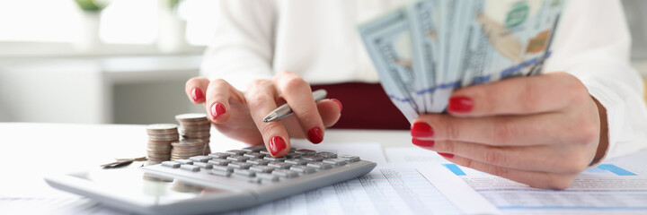 Woman holds American banknotes in her hands and works on calculator