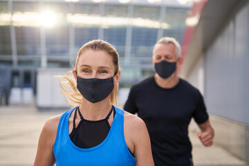 Close up portrait of sportive mature woman wearing black protective mask while running together with her husband in the morning during Covid19 pandemic