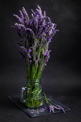 Freshly cut lavender bouquet in a glass vase on a slate with black background - 445273644