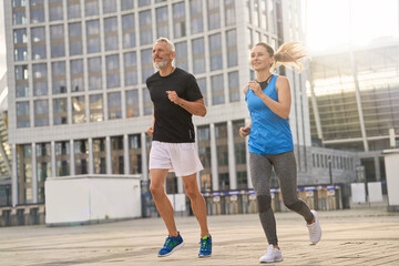 Active middle aged couple, man and woman jogging together in the morning while training outdoors