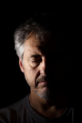 portrait of man with closed eyes in low key with half face in harsh shadows