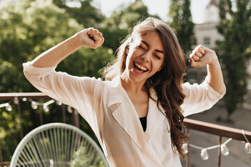 Lady in shirt having fun on balcony. Portrait of happy young woman in beige blouse sincerely...