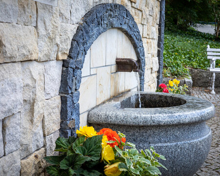 Drinking fountain surrounded with flowers. Stone basin, water running from the tap. Ladek Zdr&oacute;j mineral water health resort, Poland.