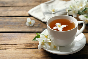 Cup of aromatic jasmine tea and fresh flowers on wooden table, space for text