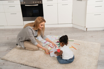 cheerful mother drawing with adopted african american girl while sitting on carpet