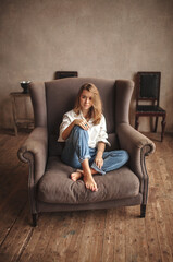 Obraz premium Attractive blond hair female sitting in armchair and looking at the camera