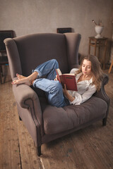 Obraz premium Young adorable woman sitting on the chair and reading book