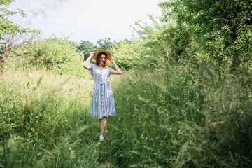 Pretty woman with sun hat walking on grass in summer park