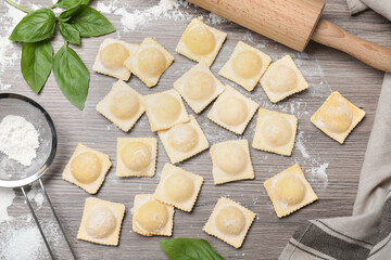 Uncooked ravioli and basil on wooden table, flat lay