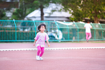 Cute Asian girl jogging at the stadium. Children wear pink t-shirts and leggings, white sneakers. Child is active, smiles sweetly, is happy. During the summer or spring. Kid aged 4-5 years old.