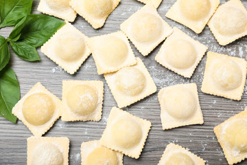 Uncooked ravioli and basil on wooden table, flat lay