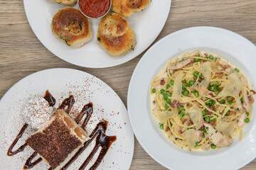 Overhead view of a 3 course meal consisting of garlic bread appetizer, chicken carbonera pasta meal, and tiramisu cake for dessert