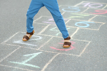 Little boy's legs and hopscotch drawn on asphalt. Child playing hopscotch game on playground on spring day.