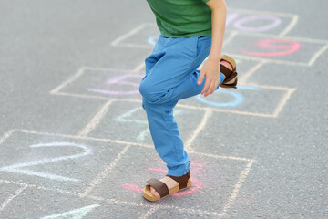 Little boy's legs and hopscotch drawn on asphalt. Child playing hopscotch game on playground on spring day.