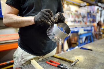 Metalwork craftsman making handmade lamp at workshop. Man worker screws up the parts of lampshade....
