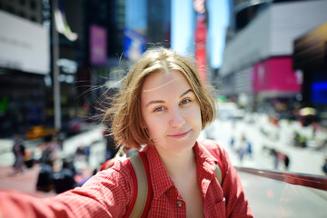 Beautiful young woman tourist taking selfie on Times Square on sunny summer day, downtown Manhattan. Famous street of New York City.