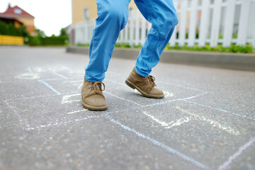 Little boy's legs and hopscotch drawn on asphalt. Child playing hopscotch game on playground on spring day.