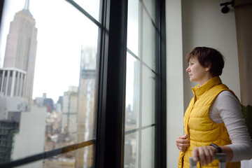 Woman tourist stays in hotel room in New York. Traveler admires of view the Empire State Building...