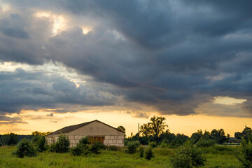 Colorful sunset with clouds in summer over a rustic farm. Summer evening landscape