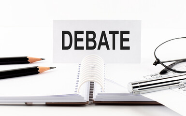 Text DEBATE on paper card,pen, pencils, glasses,financial documentation on table - business concept