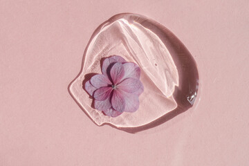 A drop of transparent cosmetic gel with flower on a pink background.