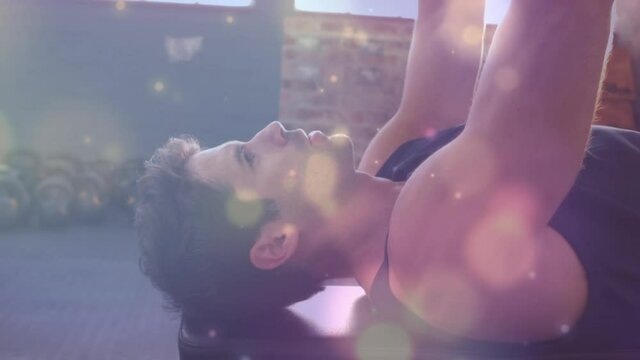 Animation of glowing light over fit man exercising in gym