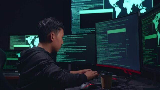 Asian Boy Hacker Hacking With Multiple Computer Screens And Pose In Dark Room
