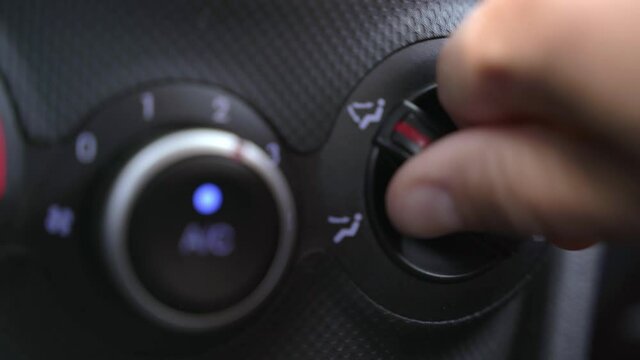 Driver hand turns lever OF heater to choose mode and air direction on black dashboard in salon of car extreme close view