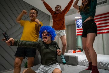 Group of Asian people friends sit on sofa watching and cheering sports games competition on TV together at home. Excited man and woman sport fans celebrate sport team victory in national sports match