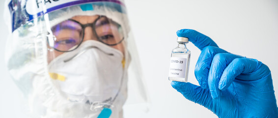 Cropped shot of healthcare worker holding and looking a bottle of covid-19 vaccine. Shot in banner size.