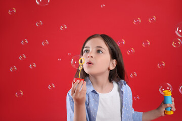 Little girl blowing soap bubbles on red background