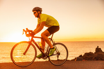 Cyclist man athlete training for triathlon riding road bike at sunset on ocean coast landscape....