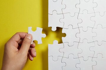 Hand holding a unfinished white jigsaw puzzle pieces on yellow background