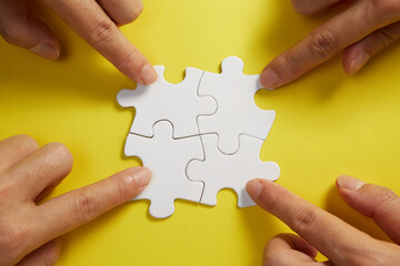 Hand joining unfinished white jigsaw puzzle pieces on yellow background