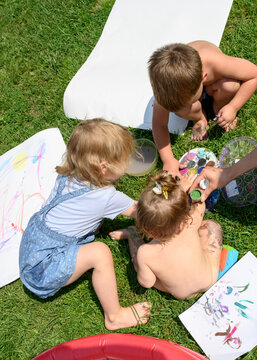 Children on the sunny lawn in front of the house paint with paints