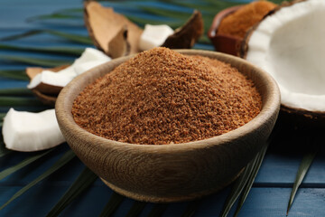 Natural coconut sugar in bowl on blue wooden table, closeup