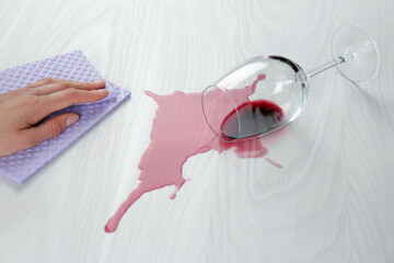 Woman cleaning spilled wine on white wooden table, closeup