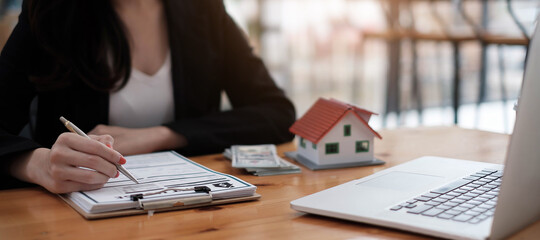 close-up view hands of businesswoman signing leasing home documents and have a house model on...