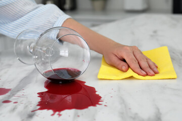 Woman cleaning spilled wine on white marble table indoors, closeup