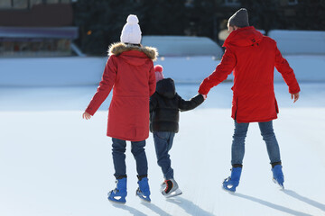 Family spending time together at outdoor ice skating rink, back view