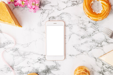 Homemade desserts, cake, profitroles and mobile phone with white screen . Eclairs with cream, French dessert and flowers on marble table on pink background
