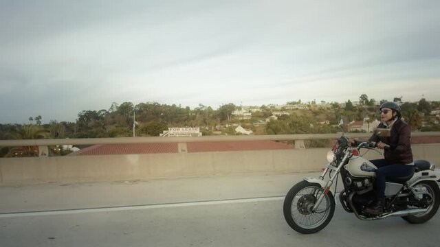 Fast push-in merging next to female motorcyclist on vintage bike on a bridge in San Diego