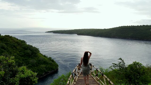 Female traveler walking to edge of wooden platform overlooking bay at sunset