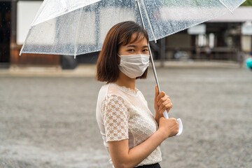 雨の中マスクを付けた若い女性