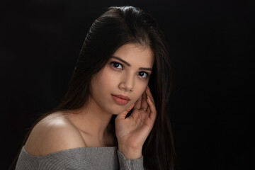 Fototapeta premium Fashion photo of a beautiful model with long hair, wearing grey top, fashion pose, studio portrait, dark background, close up pic.