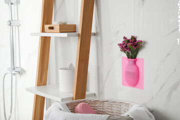 Fototapeta na wymiar Silicone vase with flowers on white marble wall in stylish bathroom