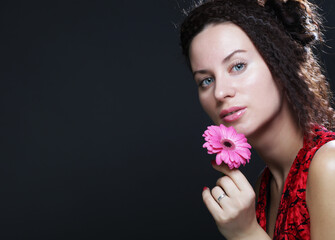 Young beautiful woman wearing red dress holding pink gerber flower
