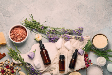 Bottle of essential oils with herbs and flowers on light gray background.