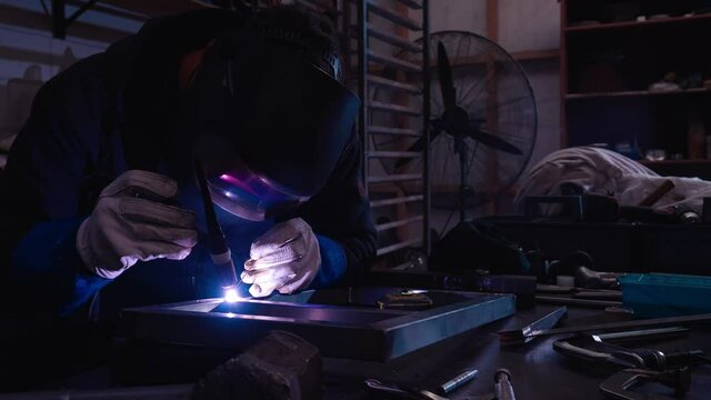 Close up of modern blacksmith using bright heat of welding machine to bind frame